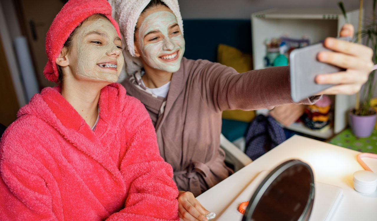 Two teenage girls doing clay face masks take a selfie.