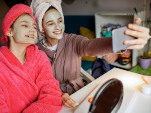 Two teenage girls doing clay face masks take a selfie.