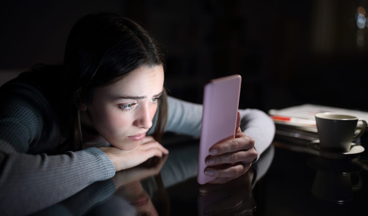 A young girl stares at a cellphone screen in a dark room. 