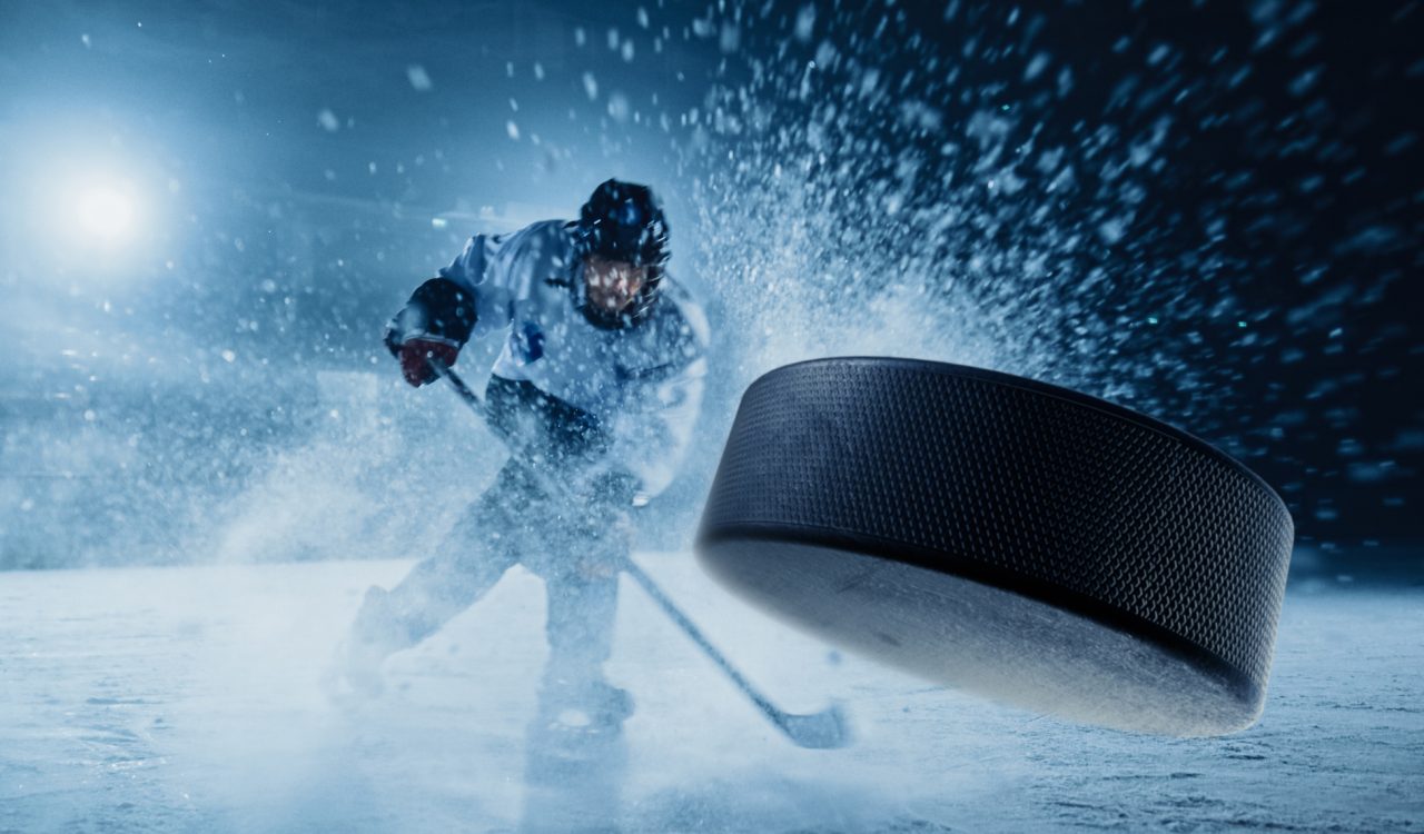 A hockey player hits a puck toward the viewer.