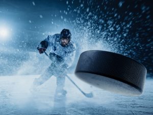 A hockey player hits a puck toward the viewer.