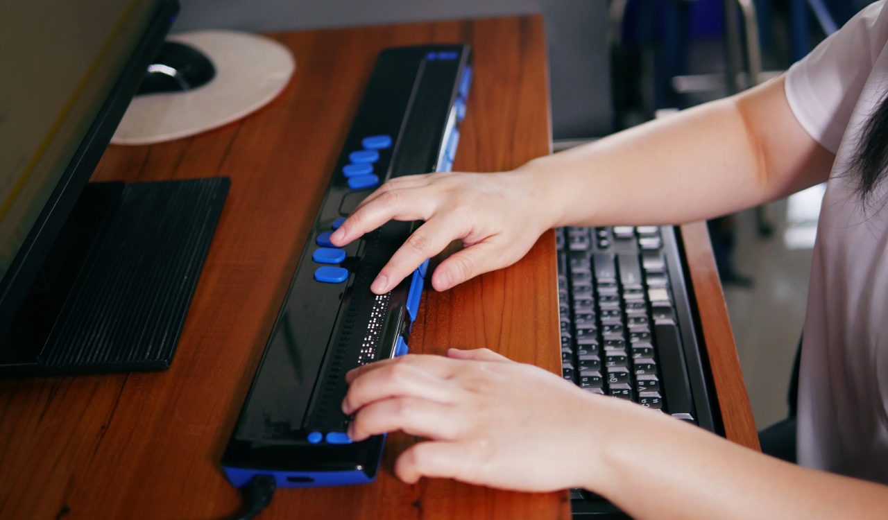 Close-up of the hands of someone using a braille terminal or display on a desk.