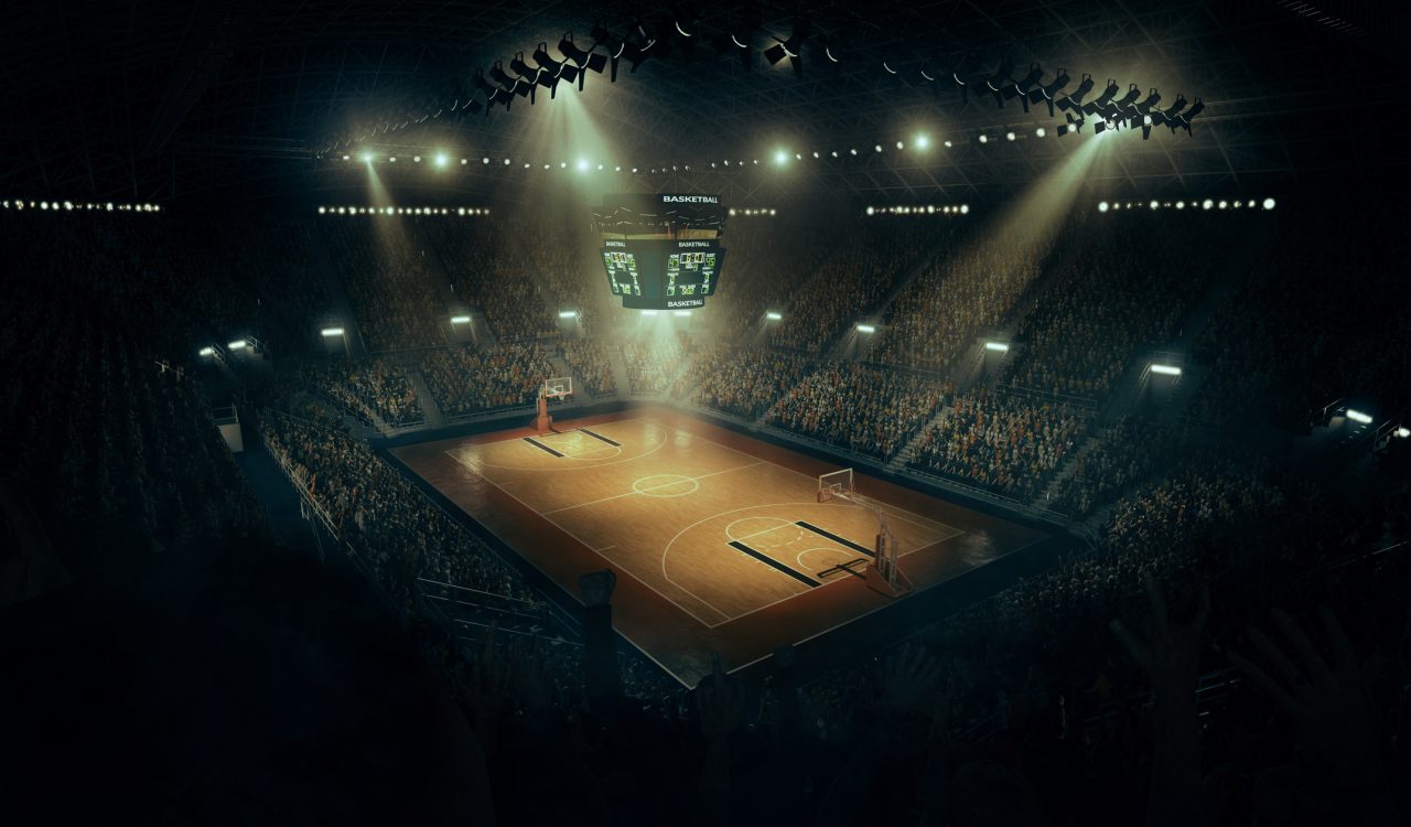 An indoor spotlit basketball arena full of spectators.