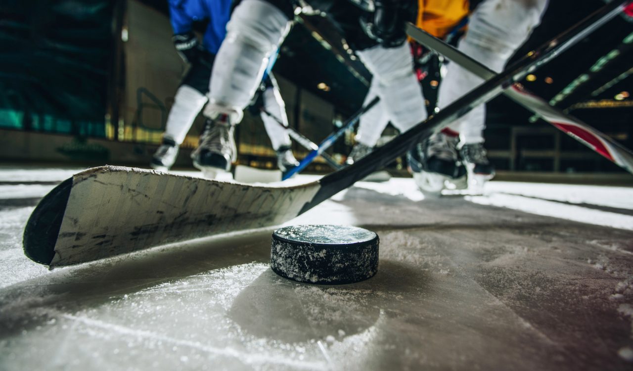 Close up of hockey puck and stick during a match with players in the background.