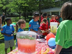 Students stand around a table selling lemonade to a customer.