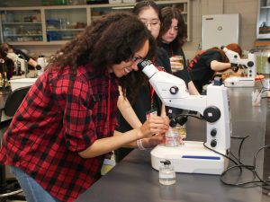 A young woman looks into a microscope to analyze a water sample.