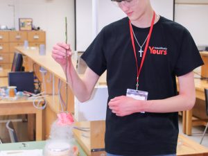 A high school student dips a cut rose into a small cylinder of liquid nitrogen.