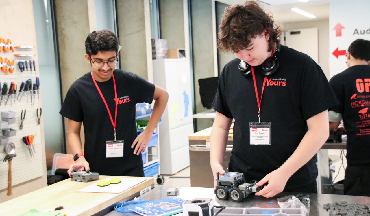 Two students build a motorized robot vehicle.