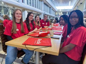 A group of teenage girls in red shirts sit at a table in a cafeteria.