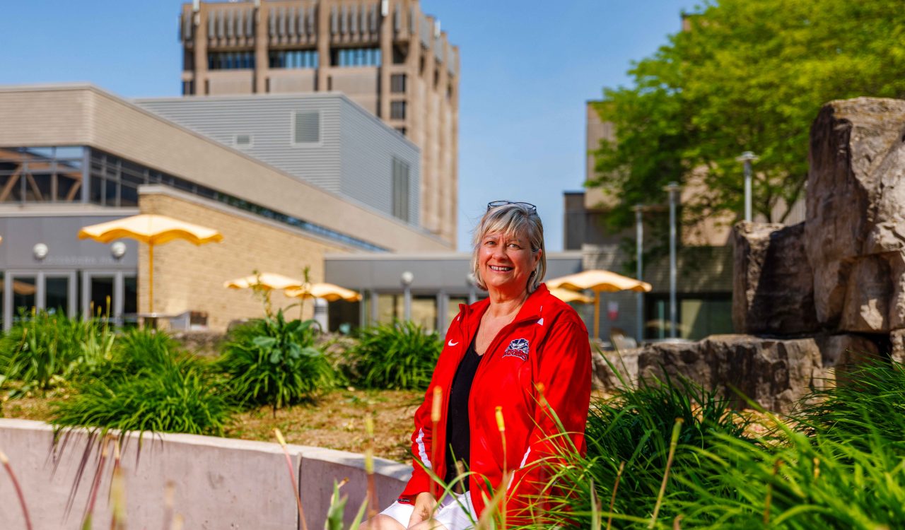 A woman sits in a garden-filled courtyard under a sunny day at Brock University.