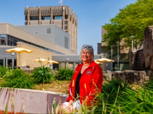 A woman sits in a garden-filled courtyard under a sunny day at Brock University.