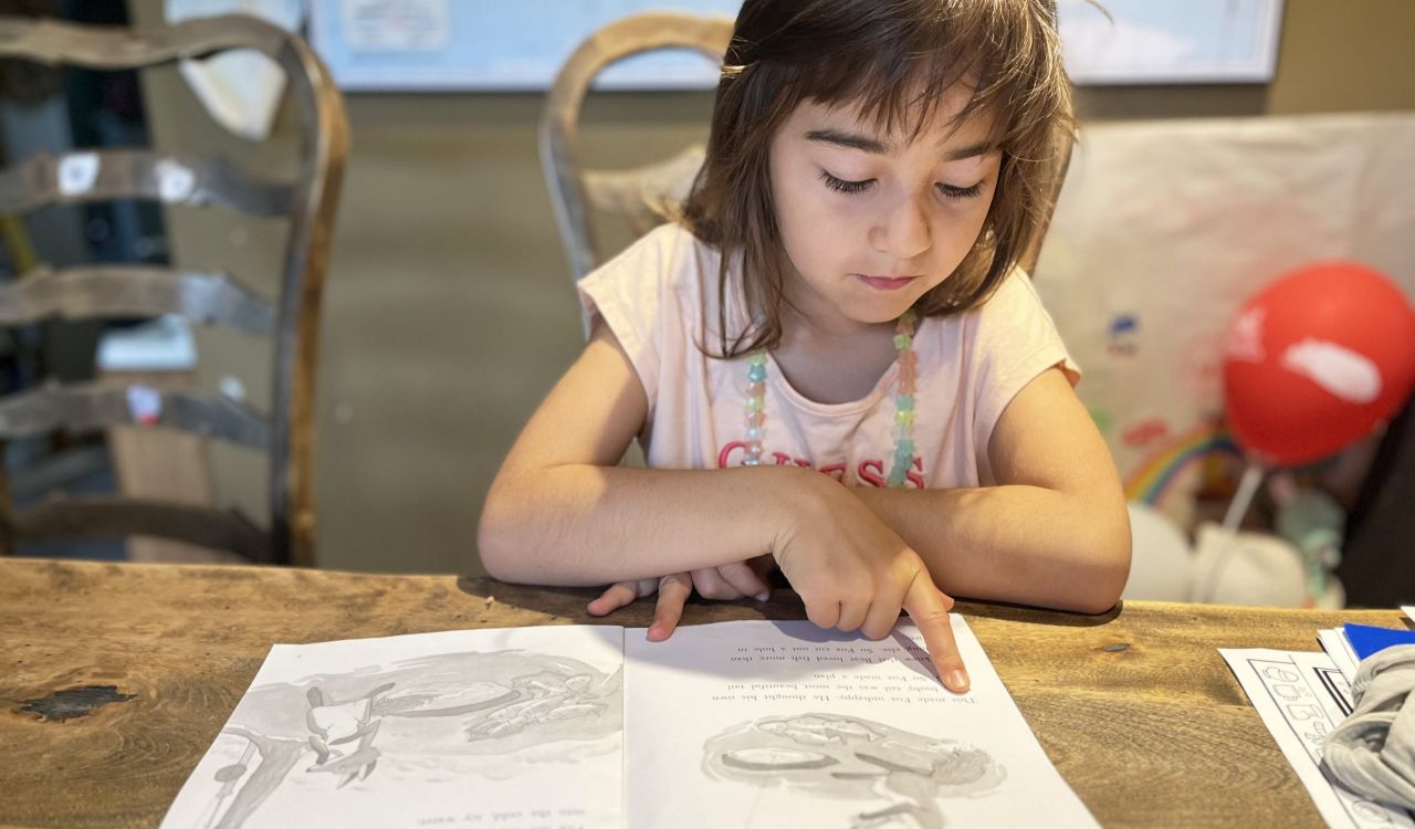 A young child sits at a table with an open book.