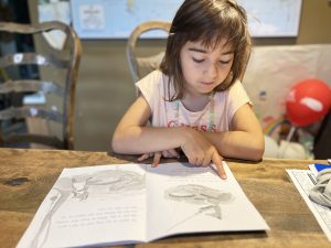 A young child sits at a table with an open book.