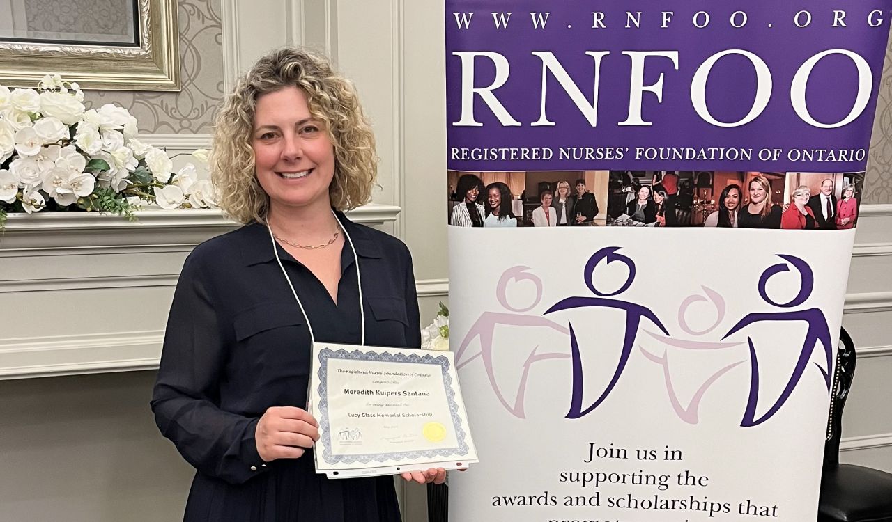 A woman holds an award certificate while standing next to a banner that reads RNFOO.