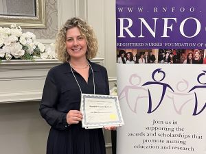 A woman holds an award certificate while standing next to a banner that reads RNFOO.