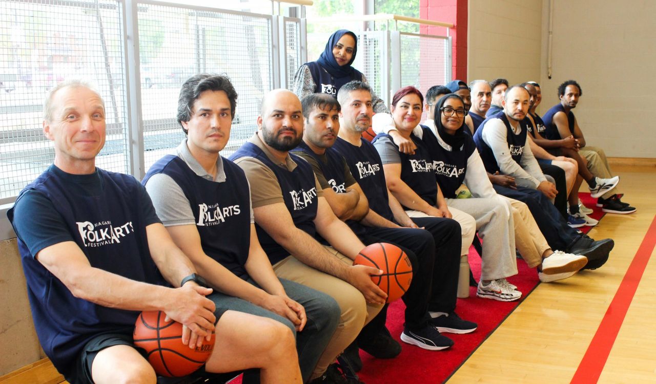 A group of people wearing basketball jerseys sit courtside at a basketball game on a team bench.