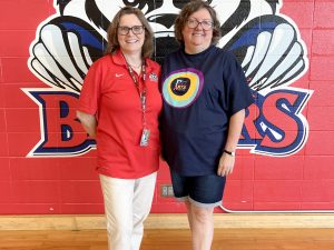 Two women pose in front of a red wall with a badger logo painted on it.