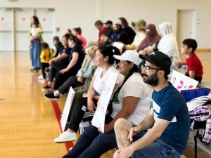 A large group of people watch a basketball game in a gymnasium.