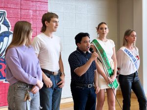 Five people stand beside each other. One is speaking into a microphone.