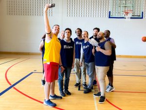 A group of basketball players take a selfie in a gymnasium.