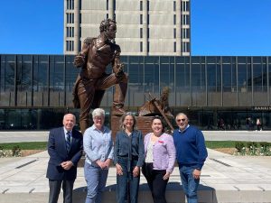 Four people pose in front of a statue and concrete and glass building.