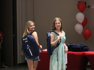 Two high school students pose for photo wearing branded backpacks at the front of an auditorium.