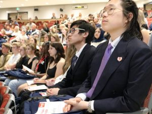 A row of high school students sit in an auditorium listening to presentation.