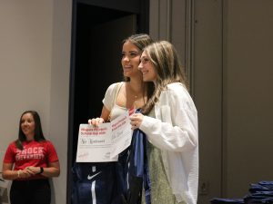 Two high school students hold award certificates and pose for photo at the front of an auditorium.