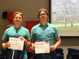 Two high school students hold award certificates and pose for photo at the front of an auditorium.