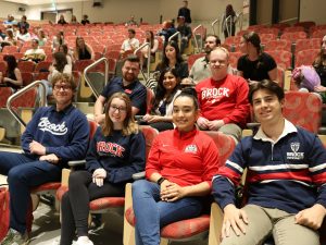 University students wearing Brock branding shirts sit together in the first row of an auditorium.