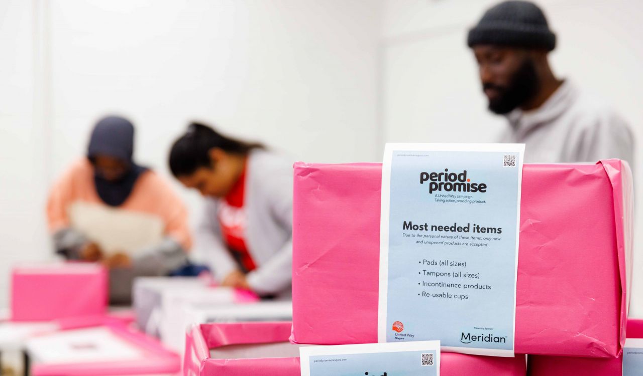 Three university students wrap cardboard boxes in pink paper.