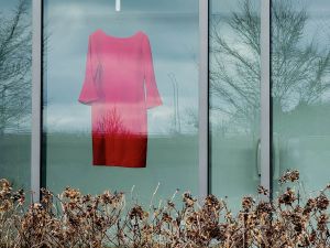 A view from outdoors shows an empty red dress hanging in the window of the Marilyn I. Walker School of Fine and Performing Arts at Brock.