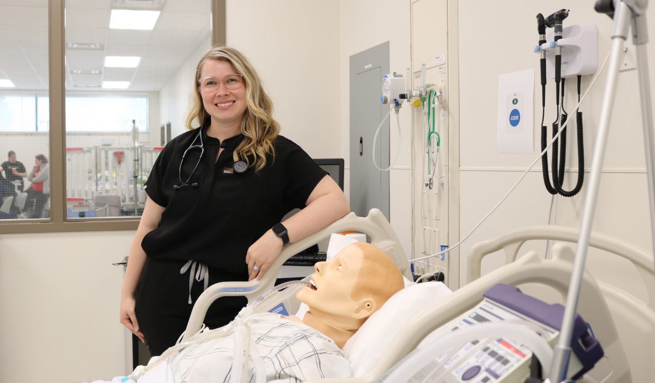 Tori McDowall stands beside a high-fidelity simulation patient in the critical care room of in Brock’s Nursing Simulation Lab.