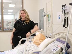 Tori McDowall stands beside a high-fidelity simulation patient in the critical care room of in Brock’s Nursing Simulation Lab.