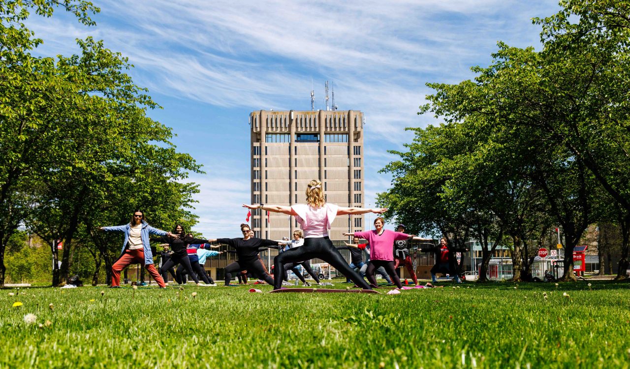 A woman leads a group of adults through a yoga session outside of Brock University.