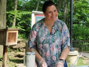 A woman stands at a picnic table, holding a knife in her hand to cut a piece of baked bannock.