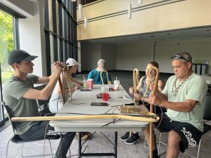 A family of five sits around a table in a conference room weaving the sting of lacrosse sticks.