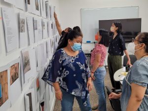 The creative team behind Ingat: An Anthology of Works by Migrant Domestic Creatives in Hong Kong studies a wall full of separate pieces during a meeting at the University of Hong Kong. Each person is masked in the conference room.