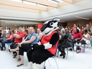 A badger mascot sits at the end of a row surrounded by seated event participants. 