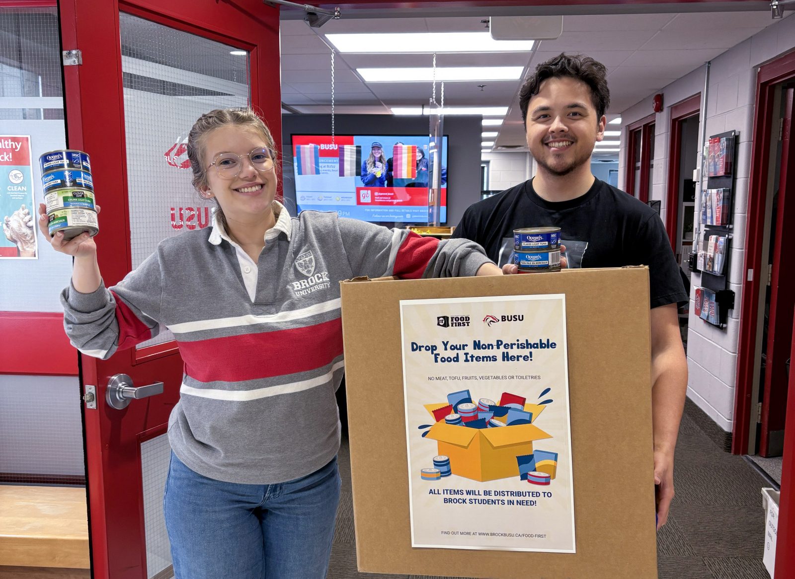 Two university students hold up a box and non-perishable food items for a photo.
