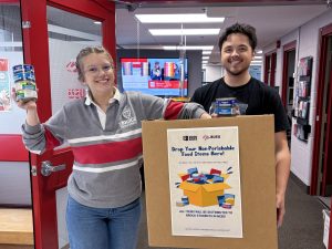 Two university students hold up a box and non-perishable food items for a photo.