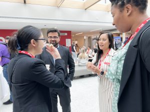 Four people stand and chat during a conference networking session in a sunny atrium.