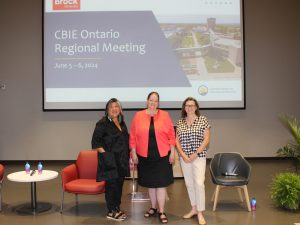 Three women pose for a picture in front of a presentation screen.