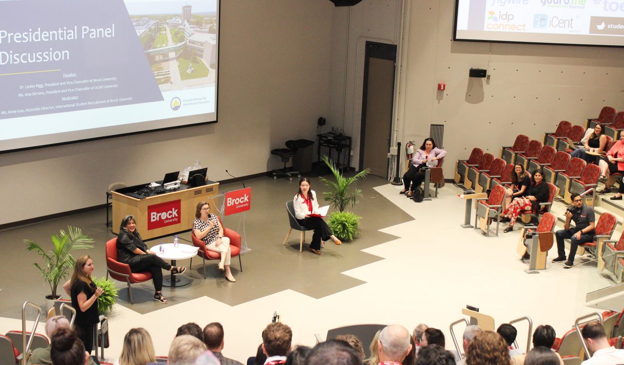 Group of panelists talk to an attendee in the audience in an auditorium.