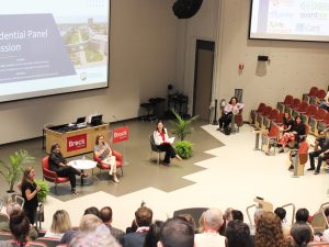 Group of panelists talk to an attendee in the audience in an auditorium.