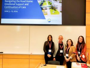 Four people pose for a picture in front of a presentation screen in a lecture hall.