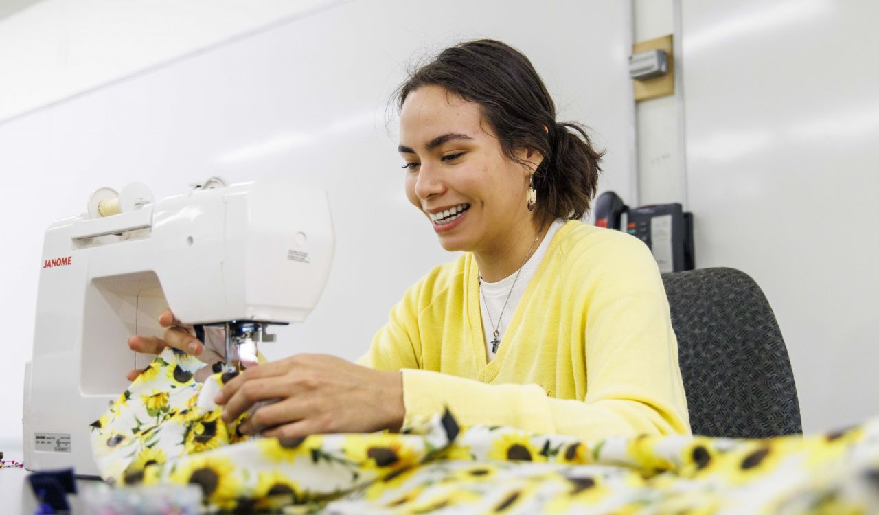 A female First Nations university student makes a traditional ribbon skirt on a sewing machine.