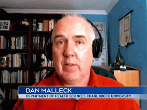 Dan Malleck wears headphones and an orange shirt while doing a video interview with CTV News in his home.