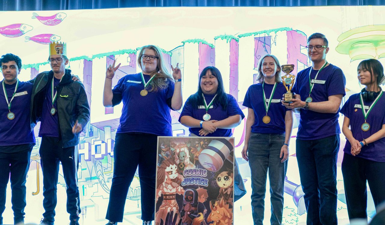 A group of Brock students wearing purple t-shirts stand on a stage in front of a brightly lit digital background. They are wearing medals and smiling at the crowd, and one person is holding a trophy.