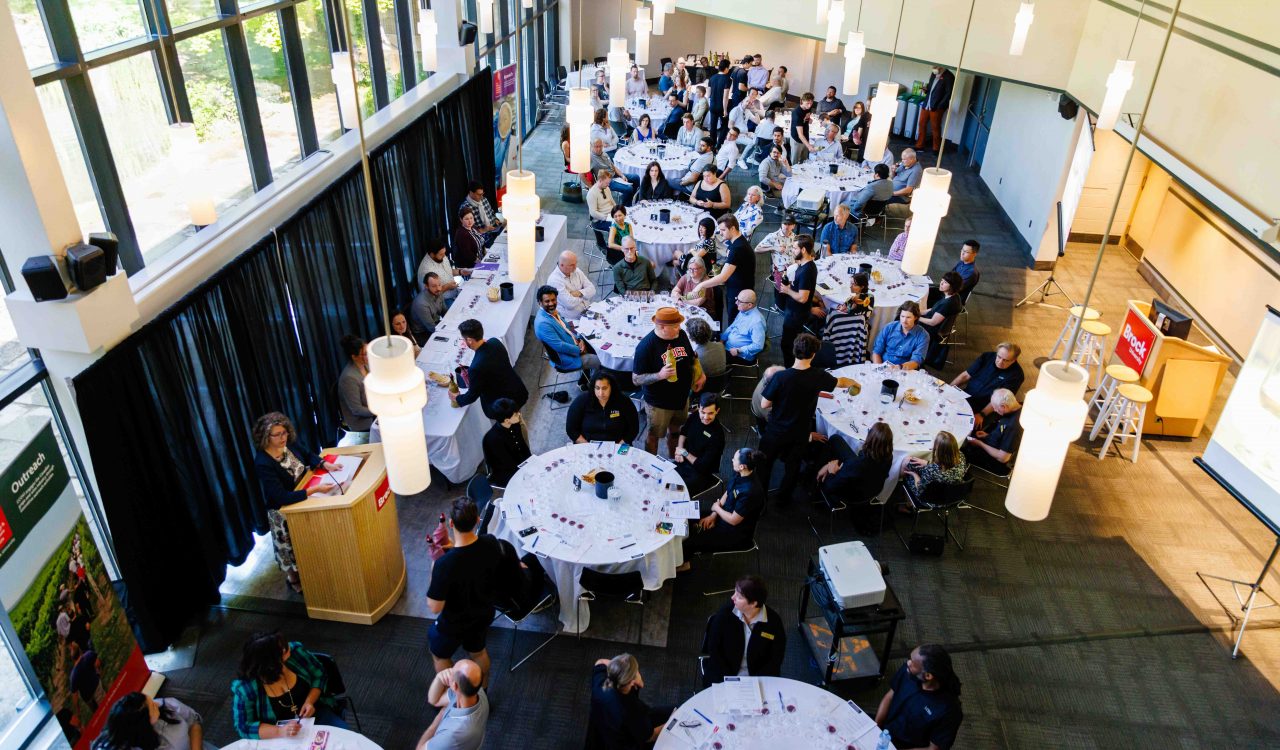 An overhead view of an event hall filled with tables and event attendees sampling wine.